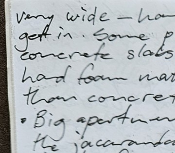 Close-up of a handwritten notebook page, showing soft-focus black ink lines on off-white paper with a brown edge of the cover visible on the left.